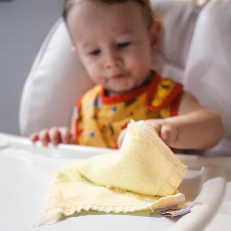a baby in a high-chair grabbing a cloth wipe