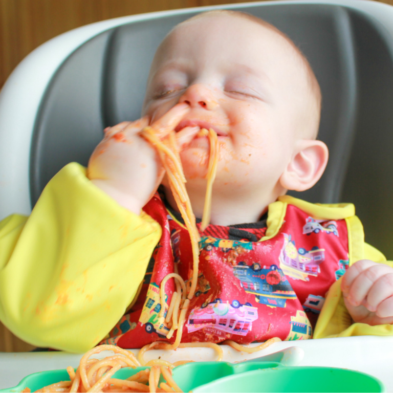 a baby eating spaghetti with a bib on