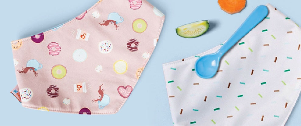 Reversible Bib laying flat next to a spoon and plate with baby food