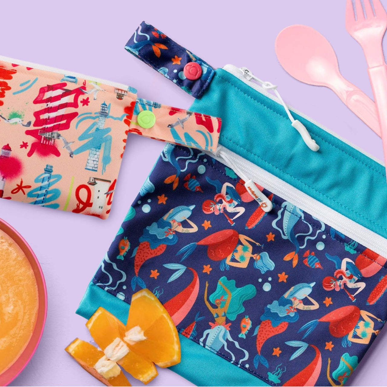 Two reusable bags next to spoon, fork and orange slices