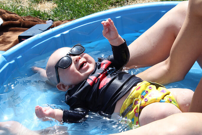 a baby floating in a pool with a fabric swim diaper and sunglasses